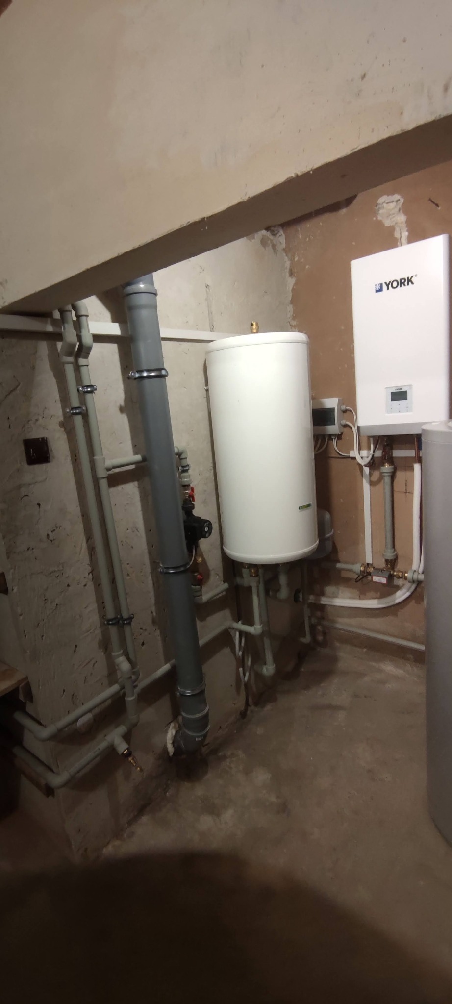 Zamontowana powietrzna pompa ciepła YORK w piwnicy, widoczne rury instalacyjne i zbiornik akumulacyjny.