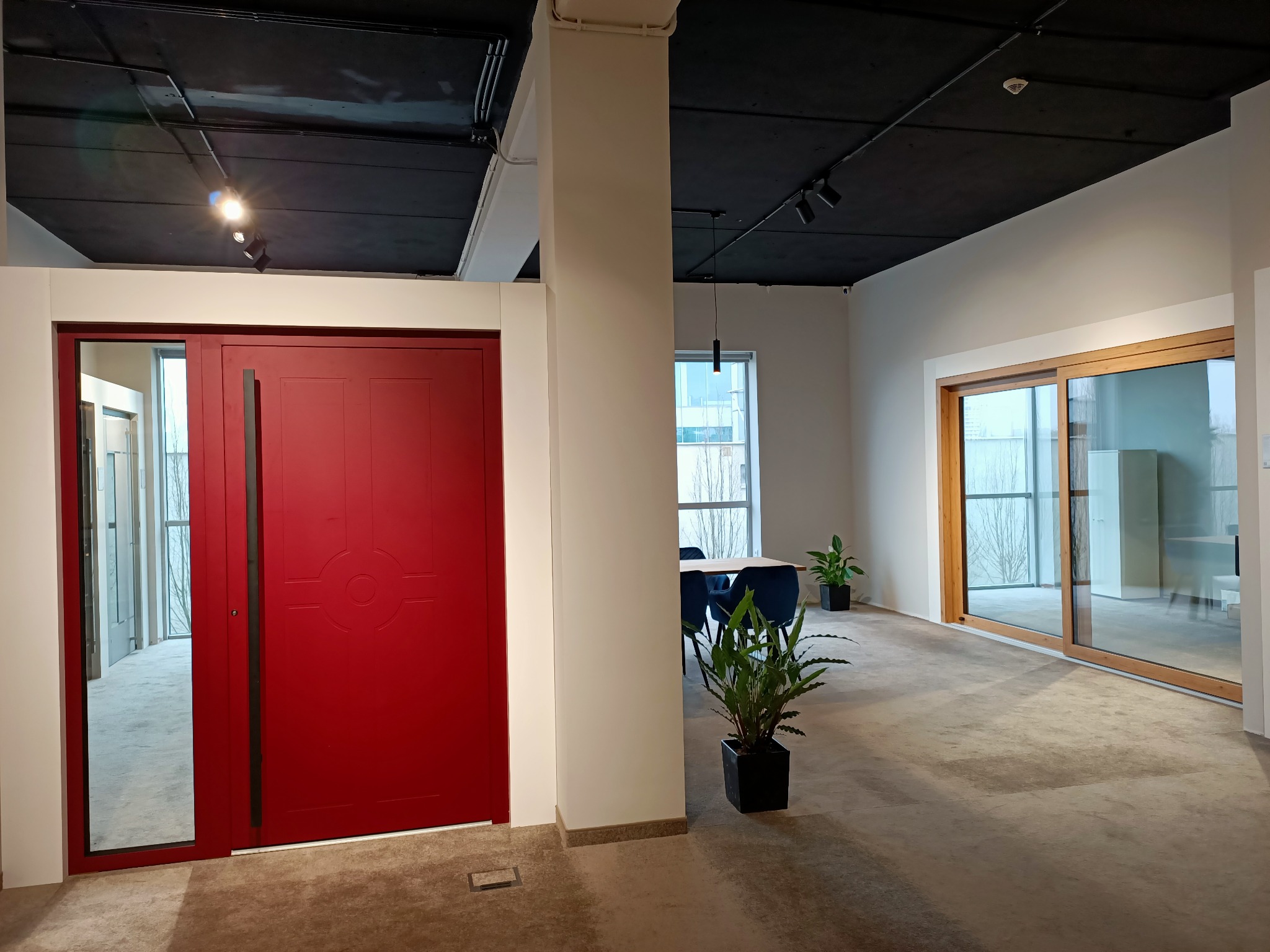 Nowoczesne wnętrze z czerwoną, przesuwną bramą drzwiową z geometrycznym wzorem, widoczne drzwi przesuwne z drewnianą ramą w tle, minimalistyczny design, czarne oświetlenie punktowe na suficie.