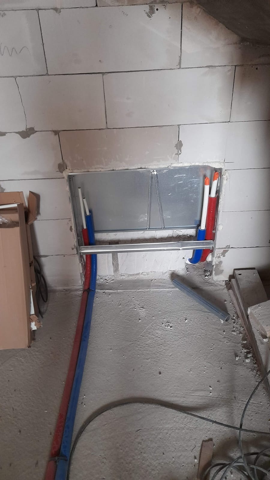 Montaż instalacji wodnej w ścianie z betonu komórkowego. Widoczne rury PEX w izolacji, metalowa rama montażowa i elementy mocujące. Surowy stan wykończenia.