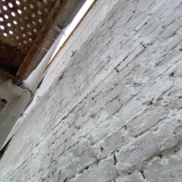 Świeżo pomalowana, biała ściana z cegły widziana z dołu, z fragmentem rusztowania po lewej stronie.