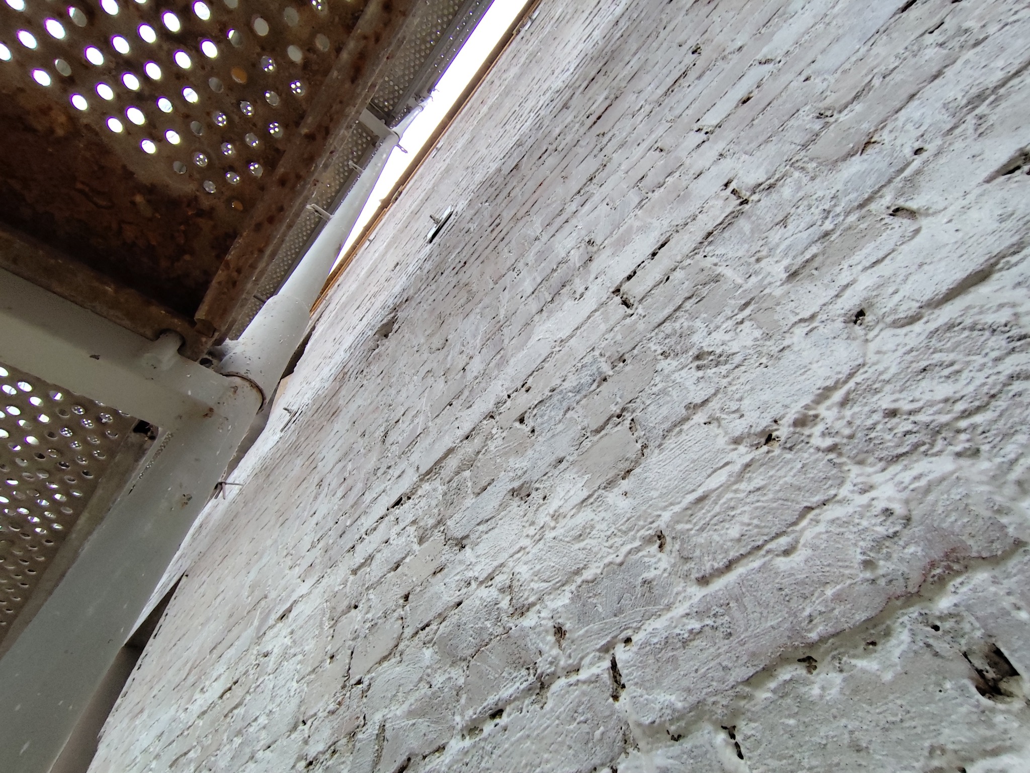 Świeżo pomalowana, biała ściana z cegły widziana z dołu, z fragmentem rusztowania po lewej stronie.