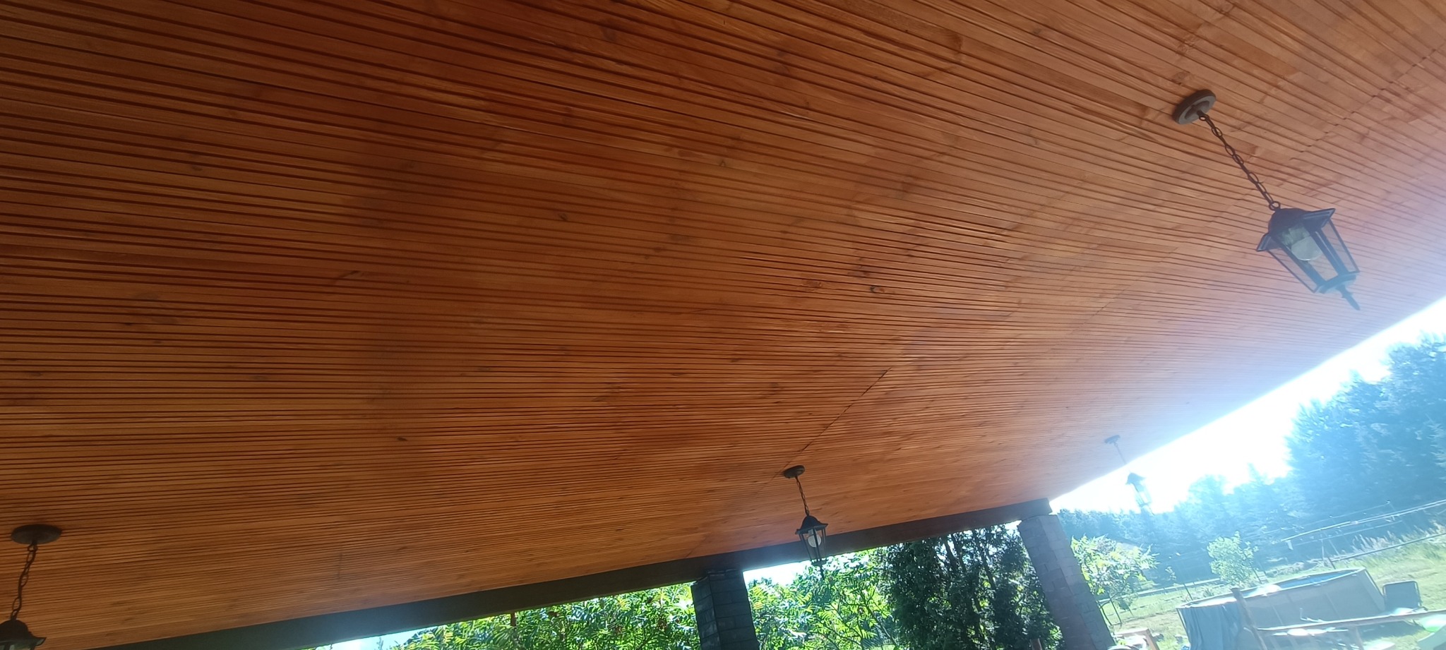 Drewniana podbitka dachowa z widocznymi lampami ogrodowymi, widok z zewnątrz, oświetlenie dzienne.