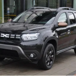 Czarny samochód Dacia Duster z brązowymi lusterkami na zewnątrz budynku z dużymi oknami.