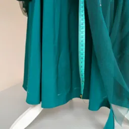 Szmaragdowa kreacja w trakcie tworzenia, z przypiętą miarką krawiecką i fragmentami tiulu, widoczne białe ślady po kredzie krawieckiej, na manekinie krawieckim.