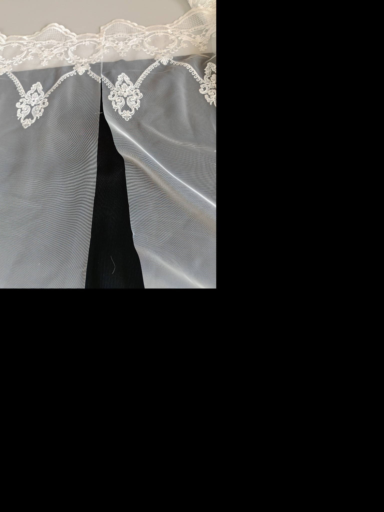 Delikatna, biała, siateczkowa firanka z koronkowym wykończeniem, z bliska, na czarnym tle.