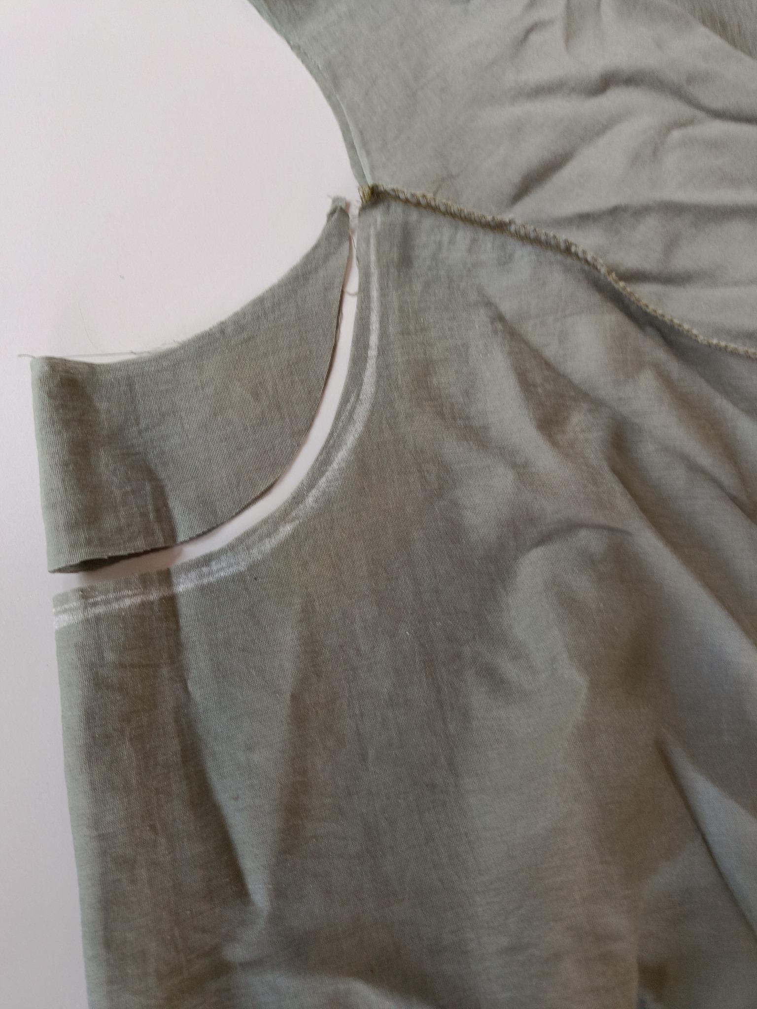 Fragment odzieży z zaznaczonym krojem i wyrysowaną linią cięcia na jasnoszarym materiale.