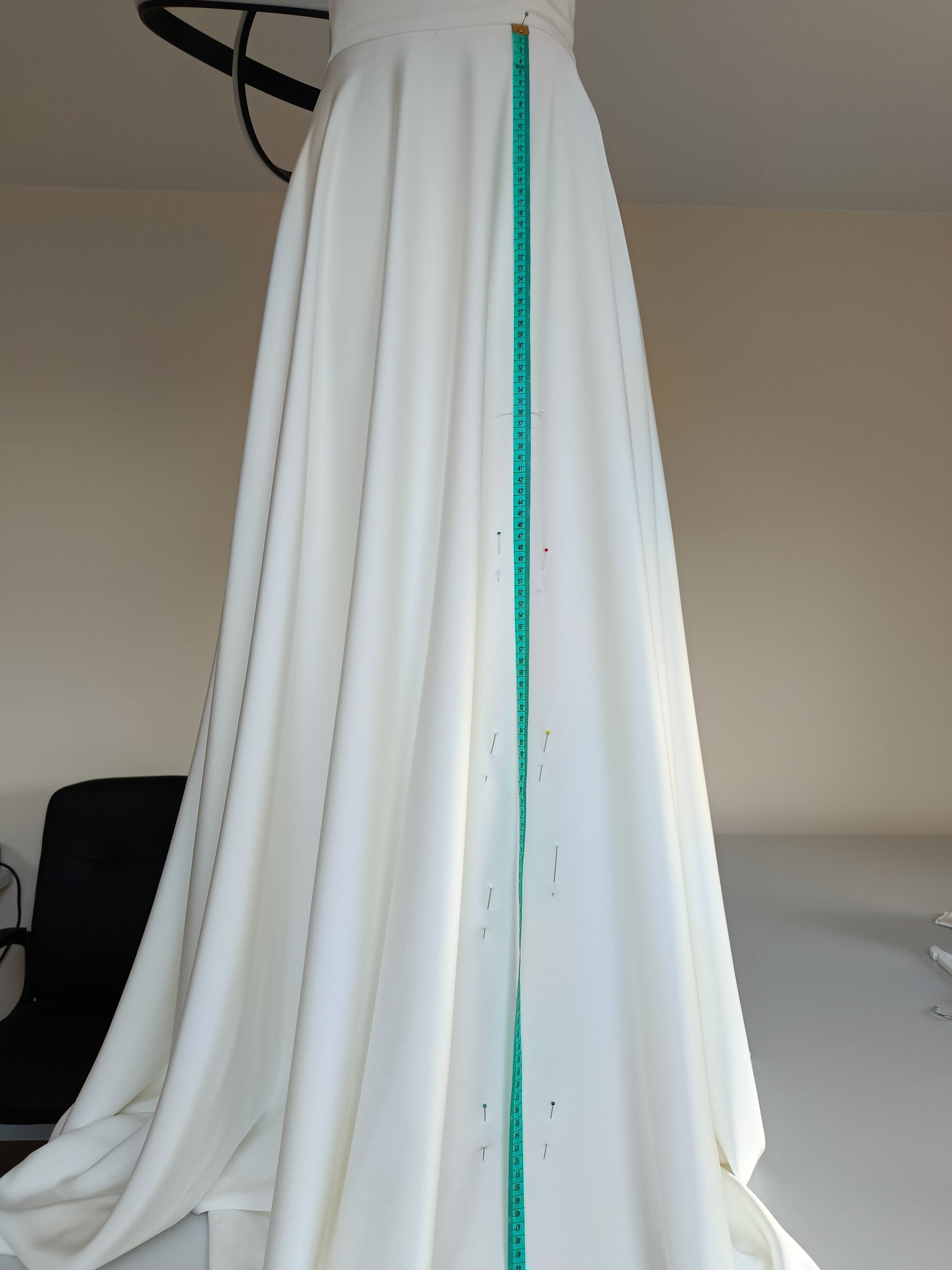 Biała suknia ślubna w trakcie dopasowywania, przypięta szpilkami i zmierzona centymetrem krawieckim.