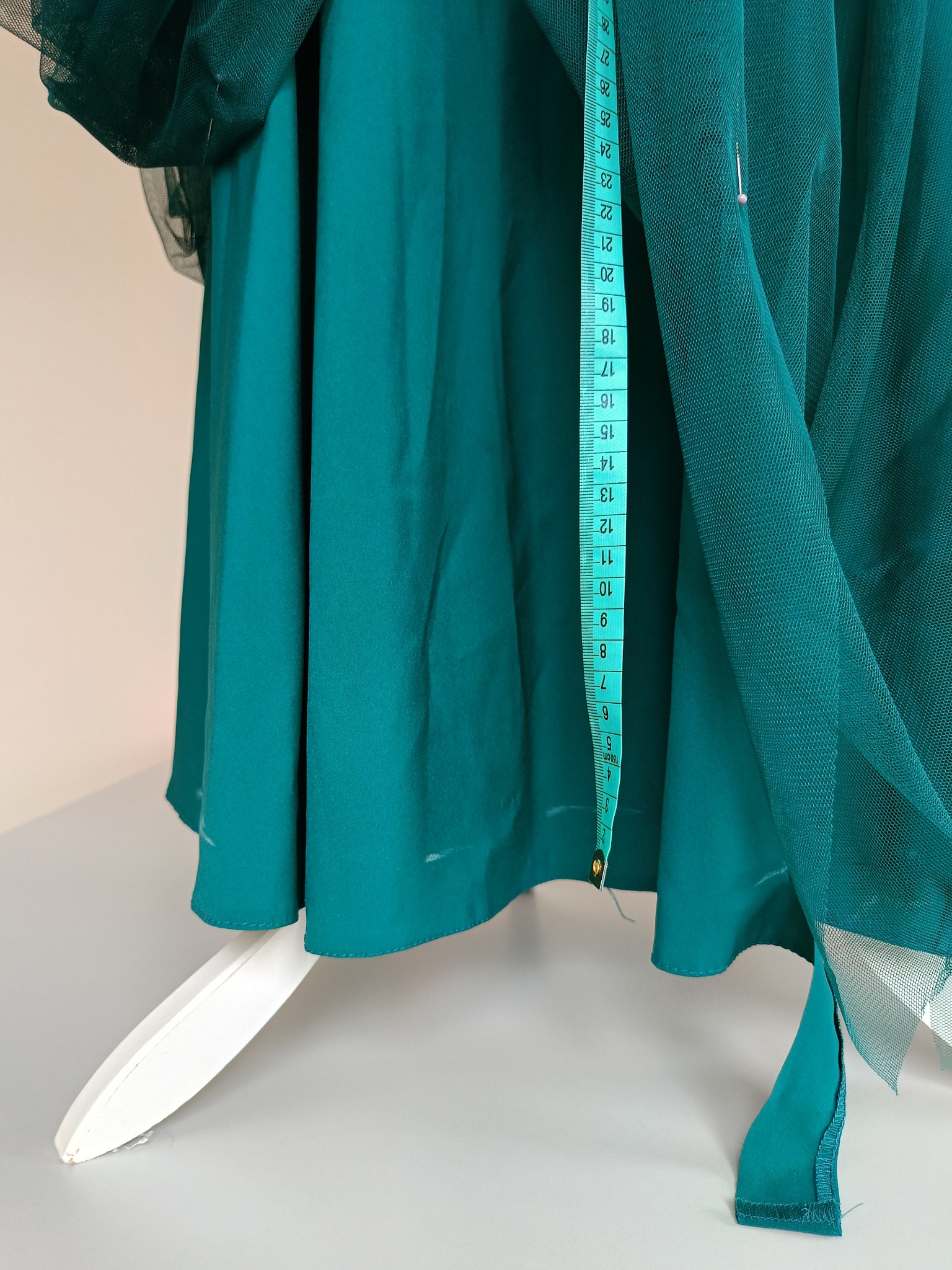 Szmaragdowa kreacja w trakcie tworzenia, z przypiętą miarką krawiecką i fragmentami tiulu, widoczne białe ślady po kredzie krawieckiej, na manekinie krawieckim.