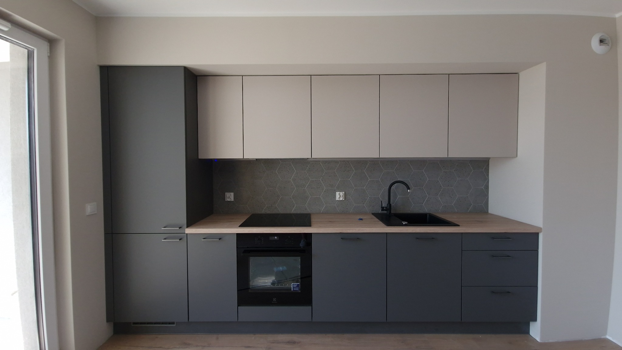 Nowoczesna kuchnia w odcieniach szarości i beżu z heksagonalnymi płytkami nad blatem, czarnym zlewem i płytą indukcyjną.