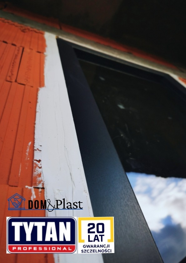 Fragment zamontowanego okna z czarną ramą, widoczna ściana z cegły i białe uszczelnienie, logo firmy Dom&Plast i Tytan Professional z 20-letnią gwarancją szczelności.