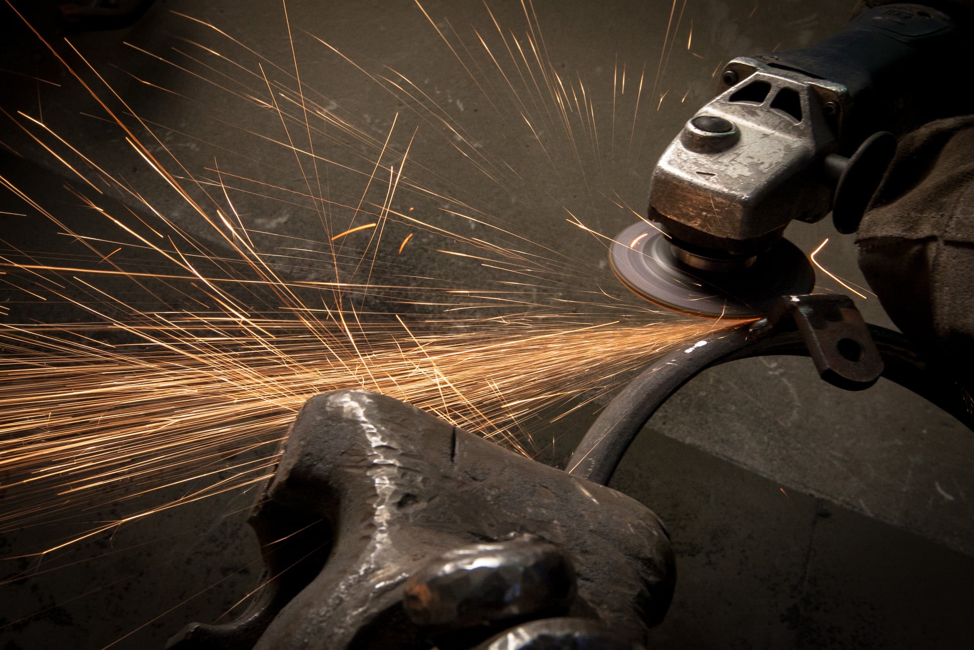 Szlifowanie metalowego elementu szlifierką kątową, widoczne iskry i rękawice ochronne.