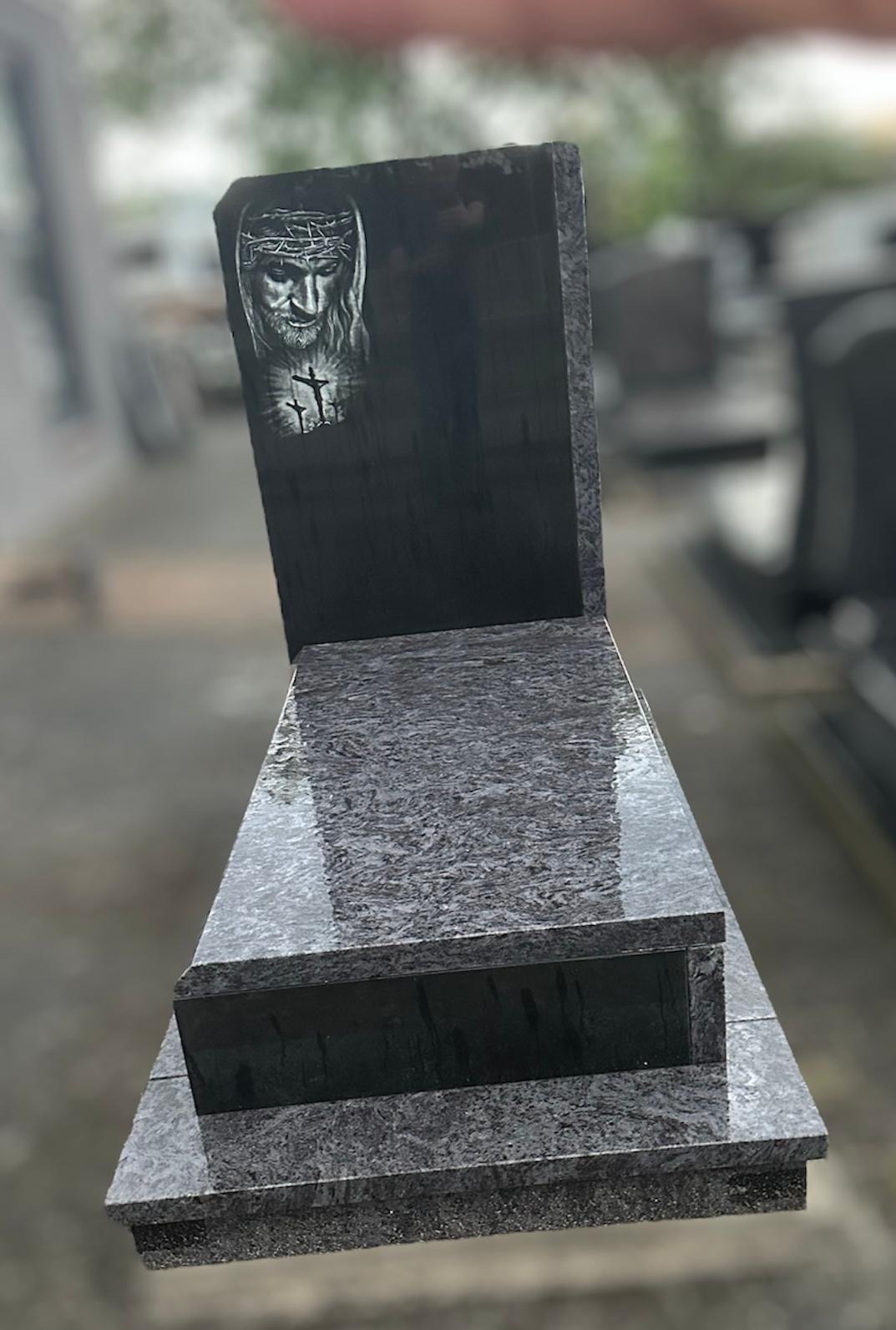 Nowoczesny, trzyczęściowy pomnik z ciemnego, wzorzystego granitu z wygrawerowanym portretem Jezusa w koronie cierniowej i dwoma krzyżami.
