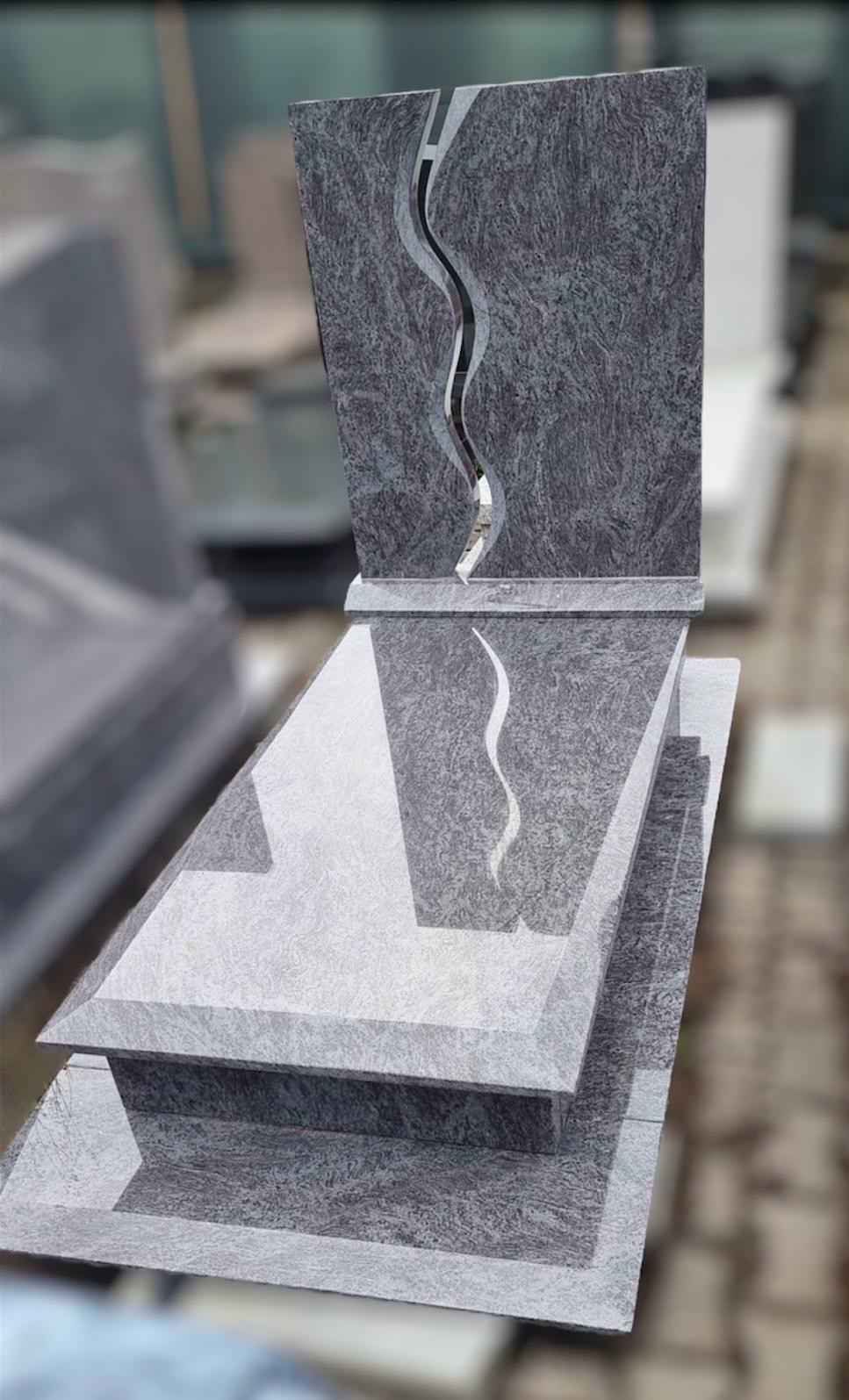 Szary nagrobek z granitu z wyciętym motywem falistym, widoczne detale obróbki kamienia i faktura materiału.