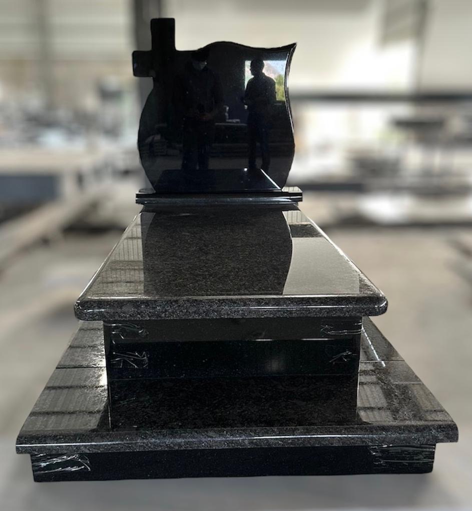 Czarny, polerowany pomnik z krzyżem, odbijający sylwetki osób w tle, ustawiony w hali produkcyjnej.