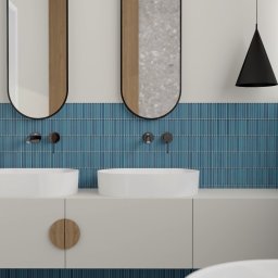 Natalia Wystup - Nowoczesna łazienka z dwoma umywalkami nablatowymi, niebieskimi płytkami w pionowy wzór, okrągłymi lustrami z czarną obwódką i drewnianymi akcentami na szafce pod umywalką.