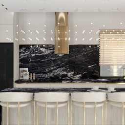 Natalia Wystup - Nowoczesna kuchnia z czarnym marmurem na ścianie, złotymi akcentami na wyspie i okapie, oraz minimalistycznym oświetleniem punktowym i wiszącą lampą z kulistych światełek.