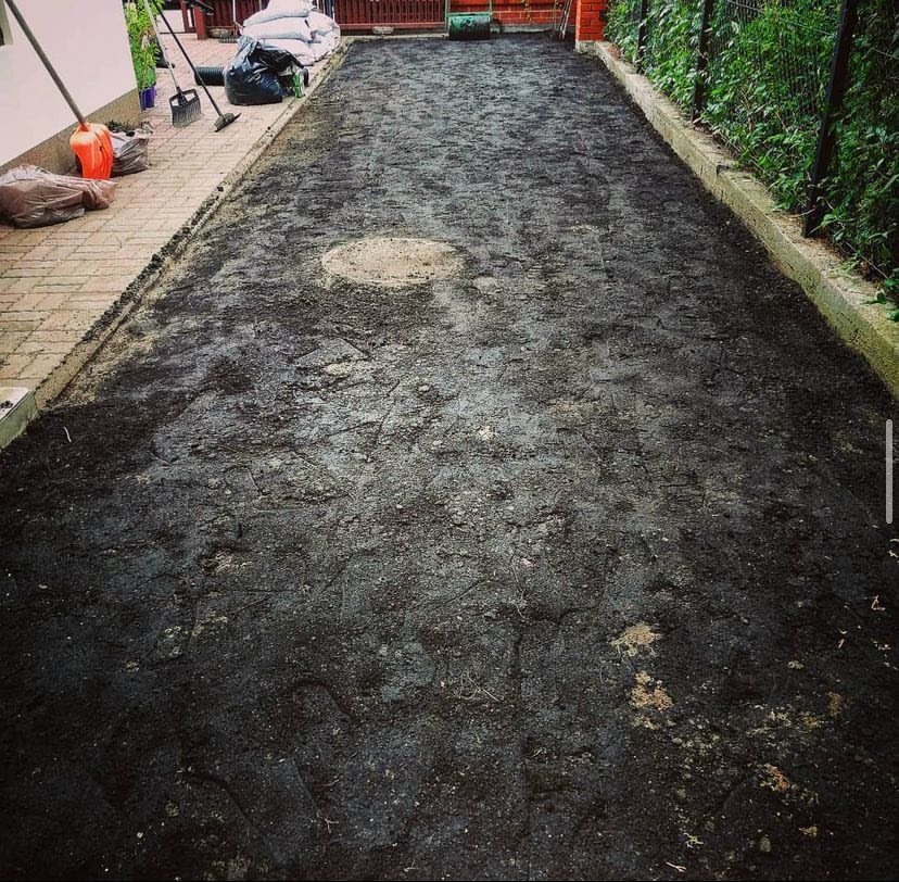 Przygotowany teren pod trawnik z widocznymi śladami po wyrównywaniu gleby, worki z ziemią i narzędzia ogrodnicze w tle.