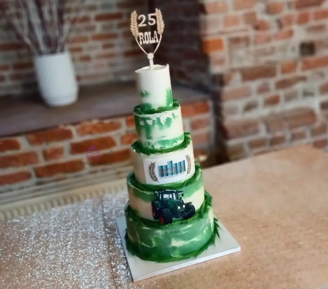 Czteropiętrowy tort w odcieniach bieli i zieleni, dekorowany motywem traktora, logiem firmy i topperem z napisem '25 Rola', ustawiony na stole z błyszczącym obrusem, w tle ceglana ściana i wazon...