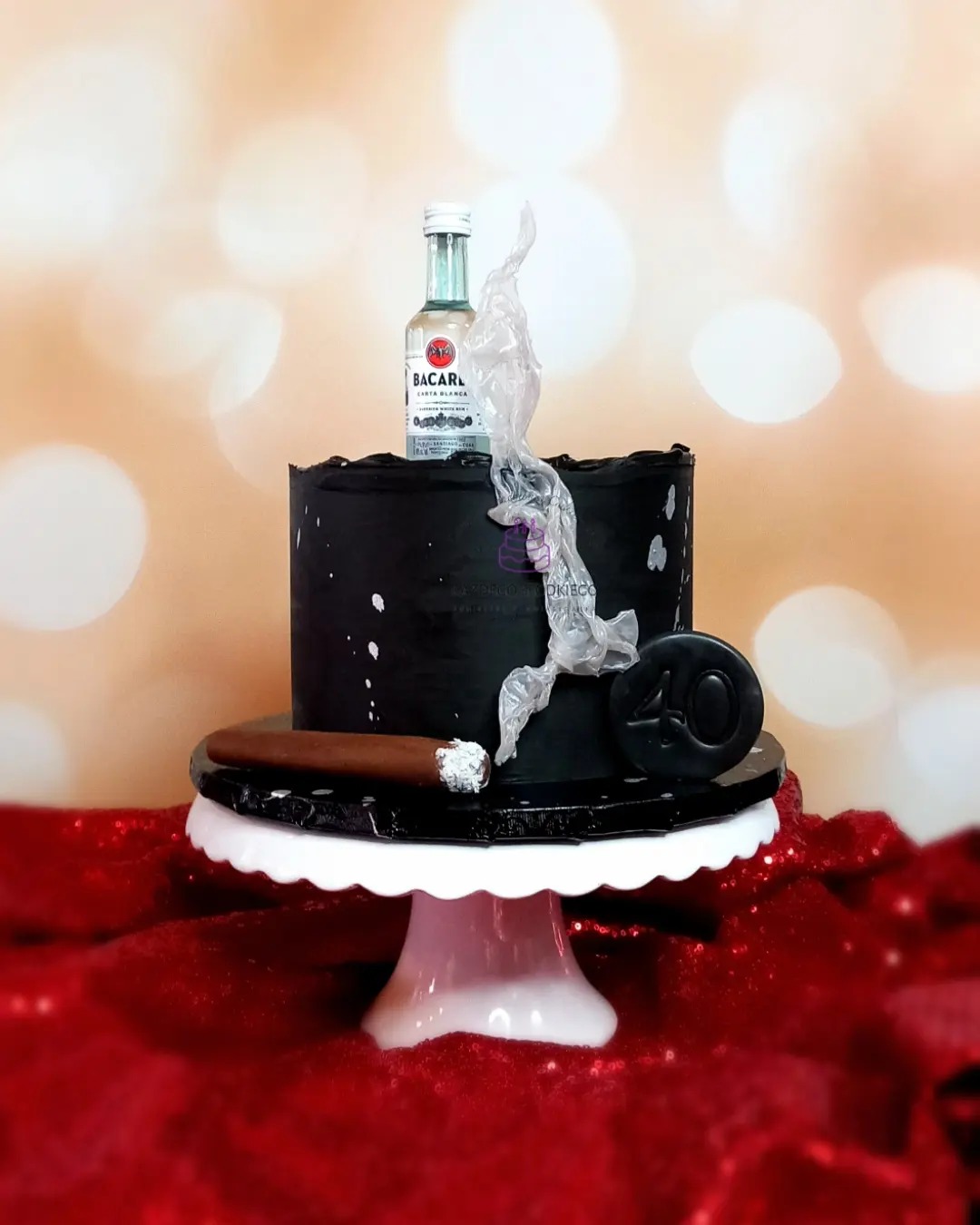 Czarny tort z dekoracjami: butelka alkoholu, imitacja cygara i liczba 40, umieszczony na białym stojaku na tle czerwonego, błyszczącego materiału.
