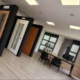 Stylowa Panorama - Wnętrze salonu z ekspozycją drzwi wewnętrznych różnych producentów (Berkado, DRE), ustawionych na podłodze wzdłuż ściany, widok na biurko obsługi klienta.