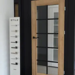 Ekspozycja drzwi wewnętrznych w salonie w Katowicach: model z drewnianą ramą i czarnymi szprosami, obok wzornik klamek.