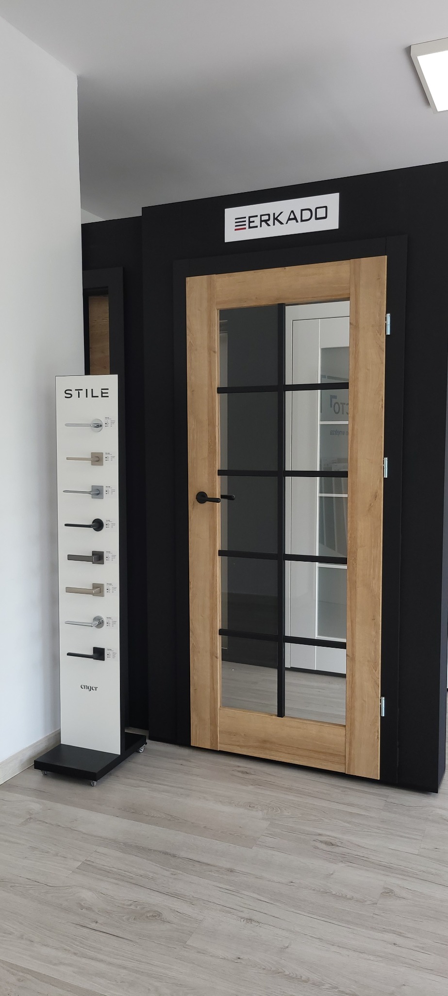 Ekspozycja drzwi wewnętrznych w salonie w Katowicach: model z drewnianą ramą i czarnymi szprosami, obok wzornik klamek.