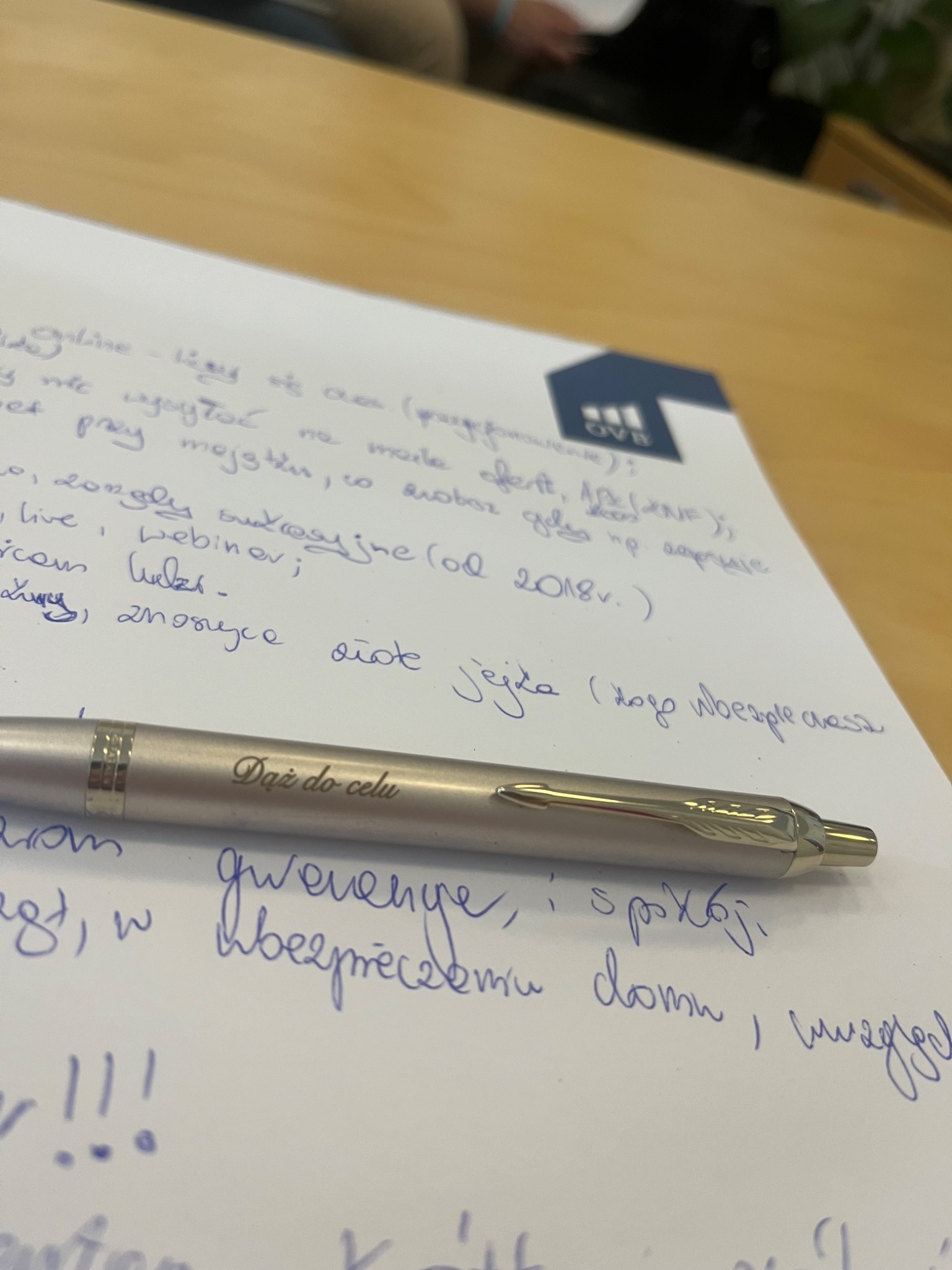 Notatki odręczne na temat usług, z długopisem Parker z napisem 'Dąż do celu' leżącym na wierzchu, obok logo firmy OVB.