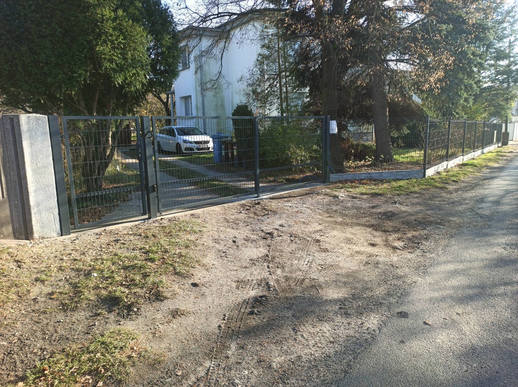 Nowoczesne ogrodzenie panelowe z bramą wjazdową, szara kolorystyka, widok na dom i podjazd z samochodem, słoneczny dzień.