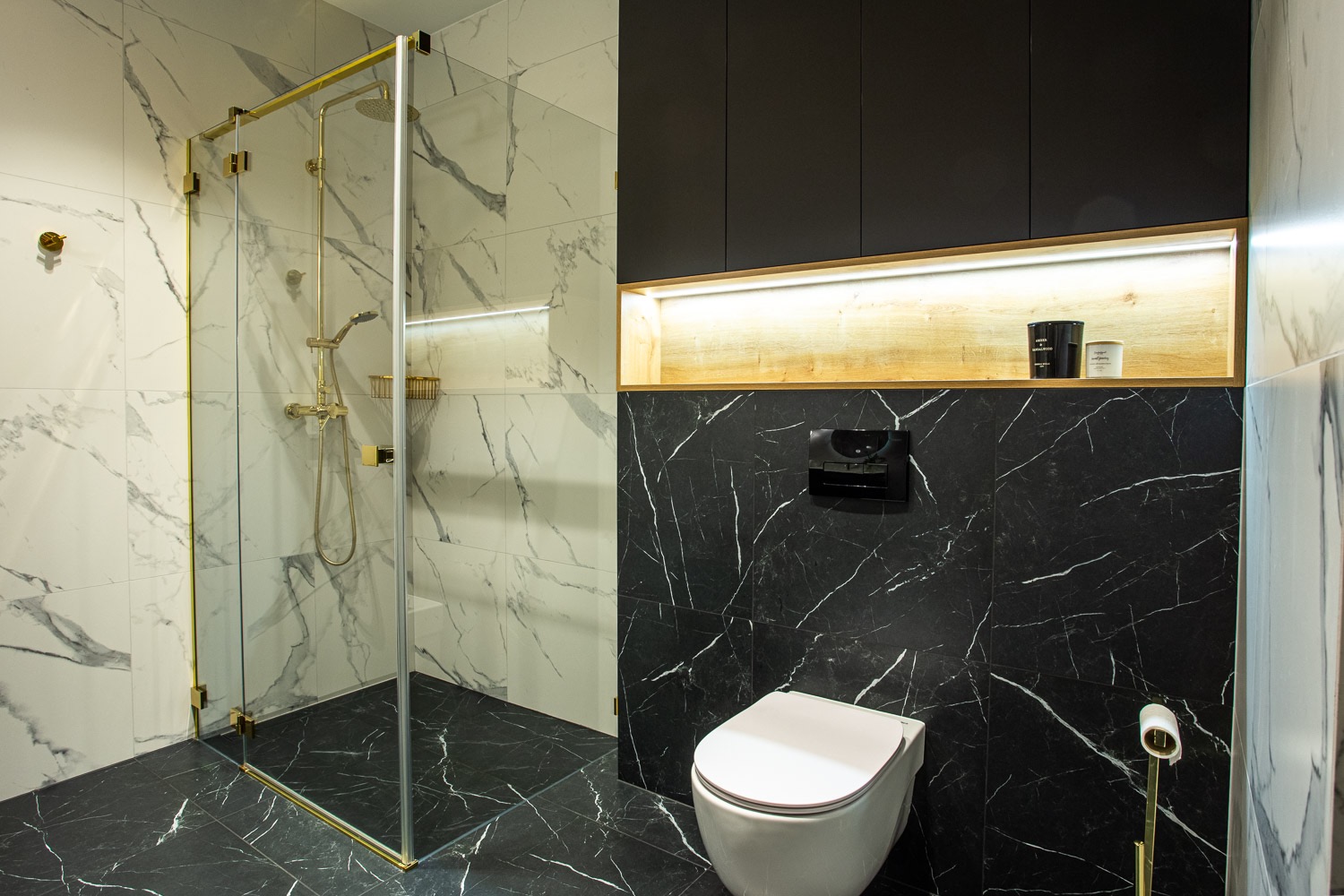 Elegancka łazienka z kabiną prysznicową ze złotymi detalami, marmurowymi płytkami i czarnymi szafkami z podświetlaną wnęką. Nowoczesny design.