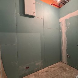 WoodyMAXX Sergiusz Proń - Ściany z płyt gipsowo-kartonowych w trakcie montażu, widoczna instalacja elektryczna i fragment instalacji wodnej, sufit z elementami wentylacji. Wnętrze w stanie surowym.