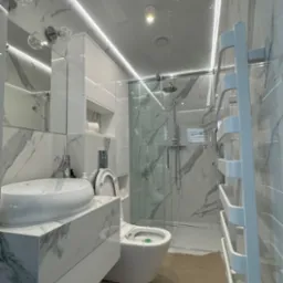 Elegancka łazienka w bieli i marmurze: umywalka na szafce, toaleta, kabina prysznicowa, grzejnik drabinkowy, oświetlenie LED. Nowoczesny design.