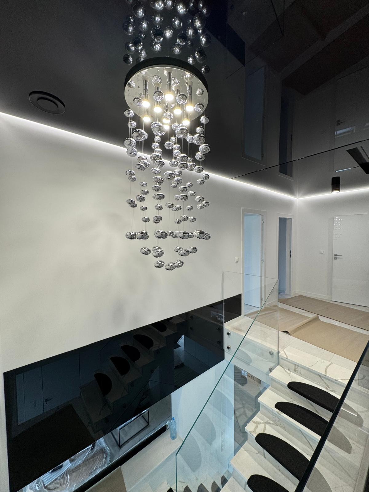 Nowoczesne wnętrze: czarny, lustrzany sufit z oświetleniem LED, kryształowy żyrandol, białe ściany i marmurowe schody z czarnymi nakładkami. Minimalizm i elegancja.