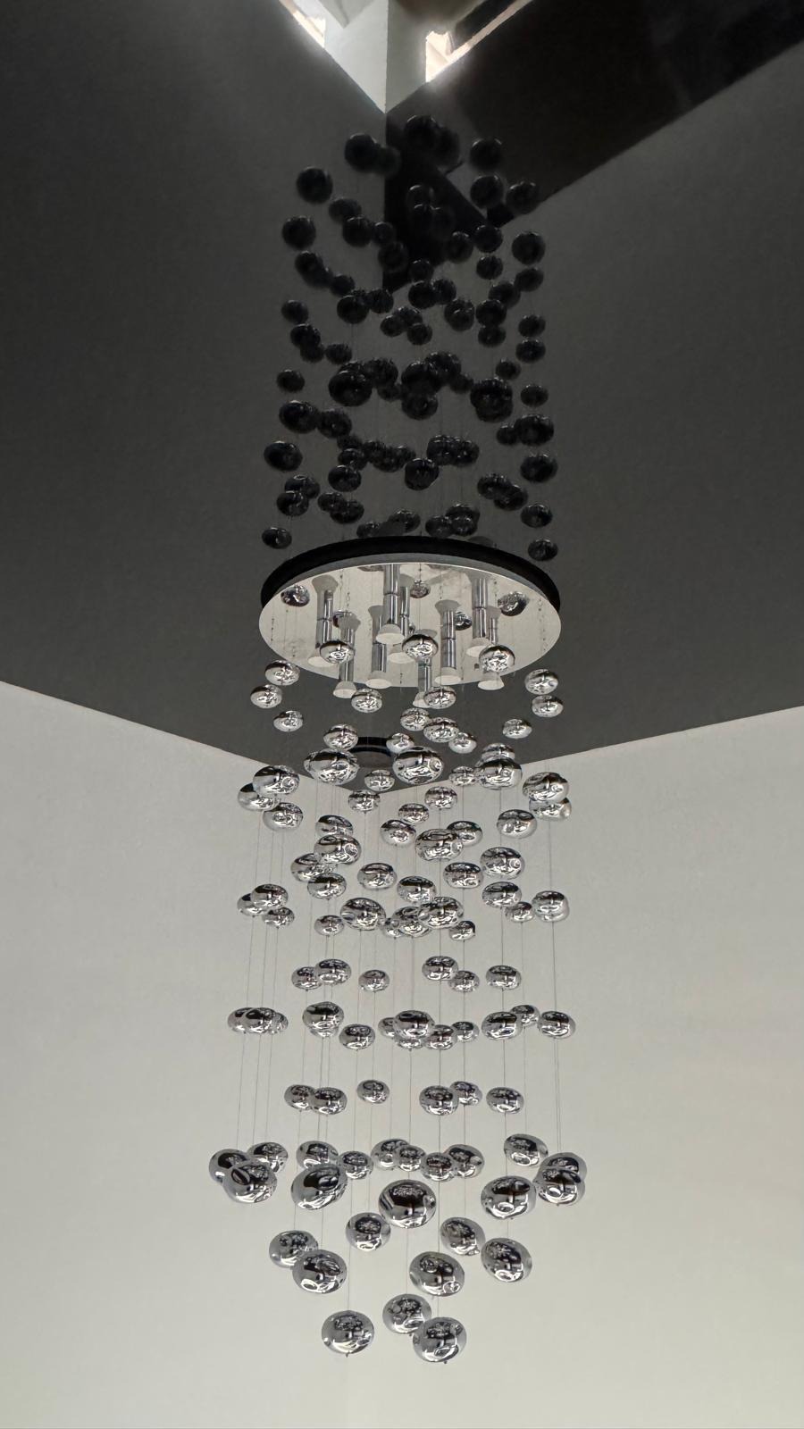 Nowoczesna lampa sufitowa z chromowanymi kulami zawieszonymi na cienkich linkach, na tle dwukolorowego sufitu (szary i biały).