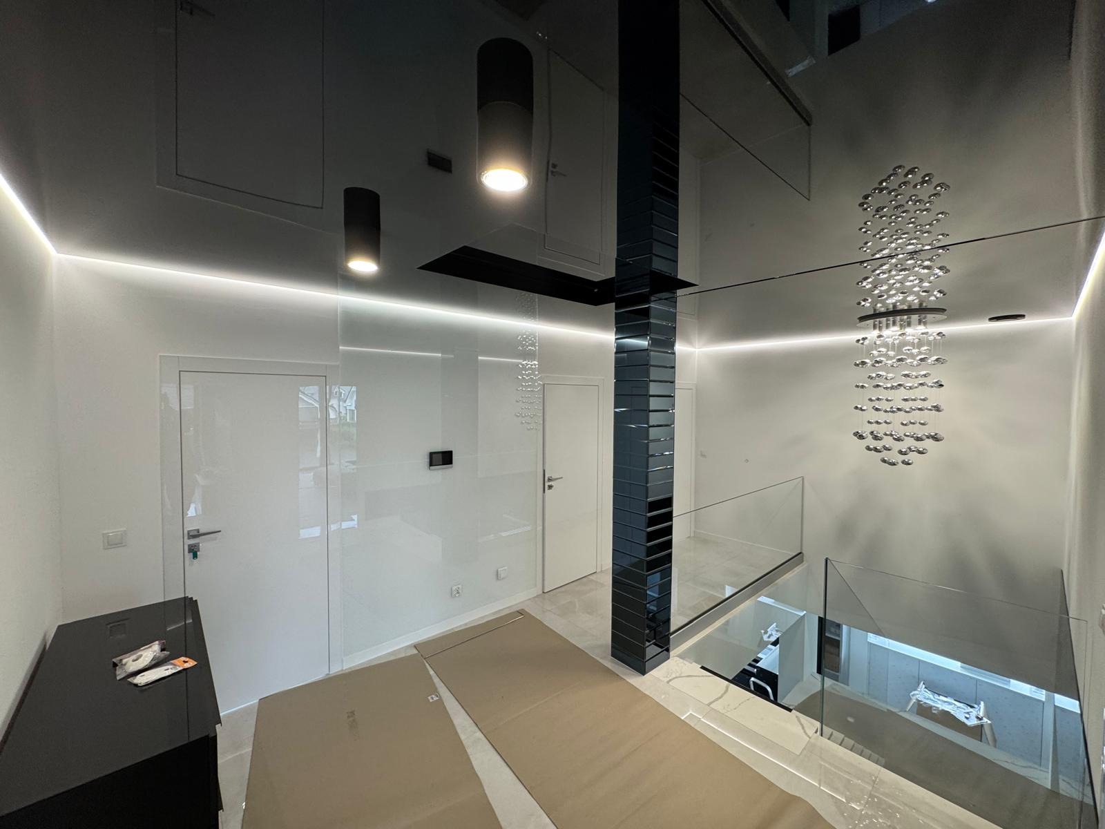 Nowoczesne wykończenie wnętrza: lśniące, białe ściany z listwami LED, lustrzany sufit i kolumna z płytek. Na podłodze kartony zabezpieczające.