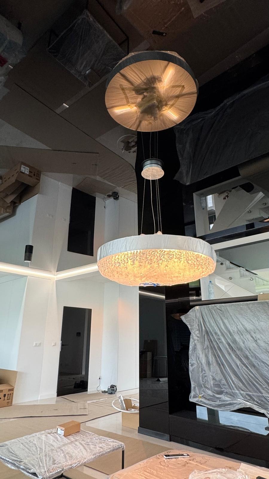 Nowoczesne lampy wiszące w jasnym wnętrzu, meble zabezpieczone folią ochronną, widoczne elementy wykończeniowe.