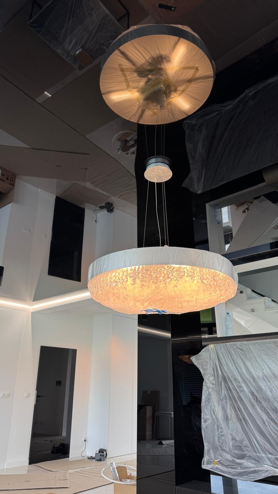 Nowoczesne wnętrze w trakcie wykończenia: okrągłe lampy wiszące, zabezpieczone folią elementy, czarne lustrzane panele i białe ściany. Widoczne przygotowania do prac.