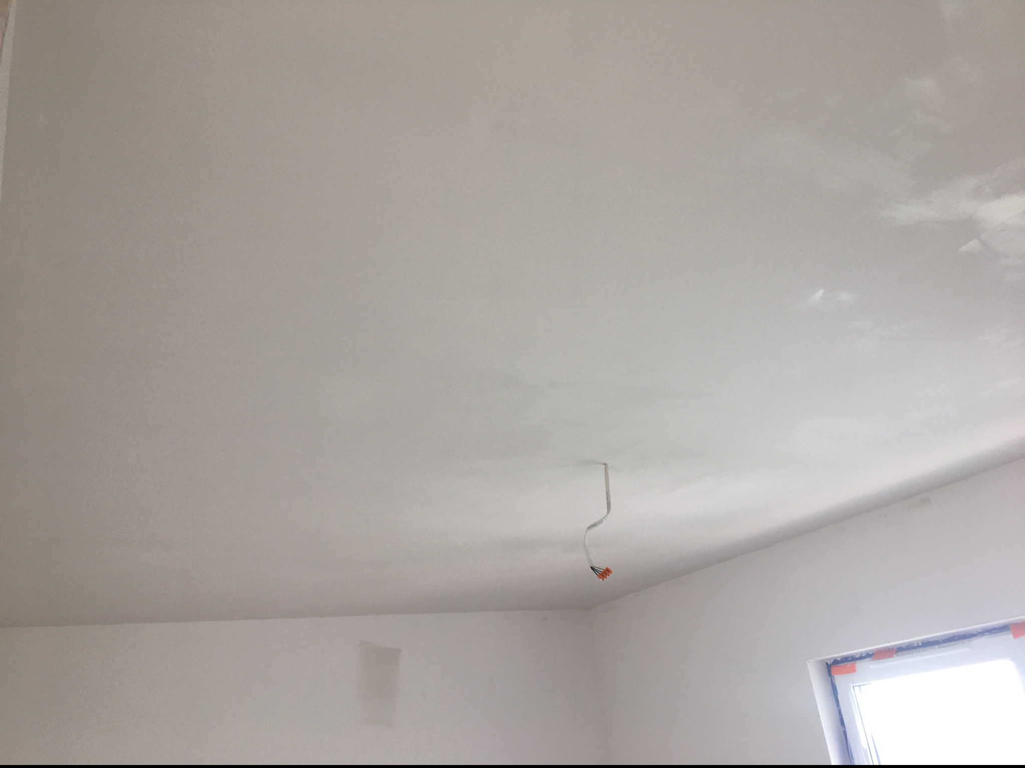 Gładki, biały sufit po szpachlowaniu z wystającym przewodem elektrycznym i fragmentem okna w rogu pomieszczenia.
