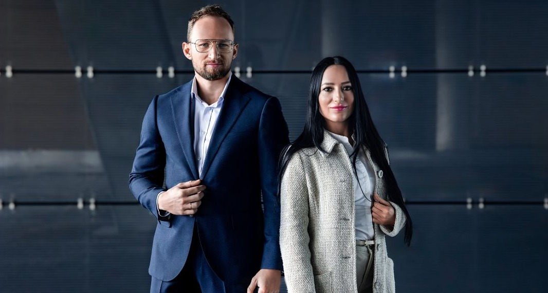 Profesjonalny portret dwójki doradców w eleganckich strojach na tle nowoczesnej ściany biurowej.