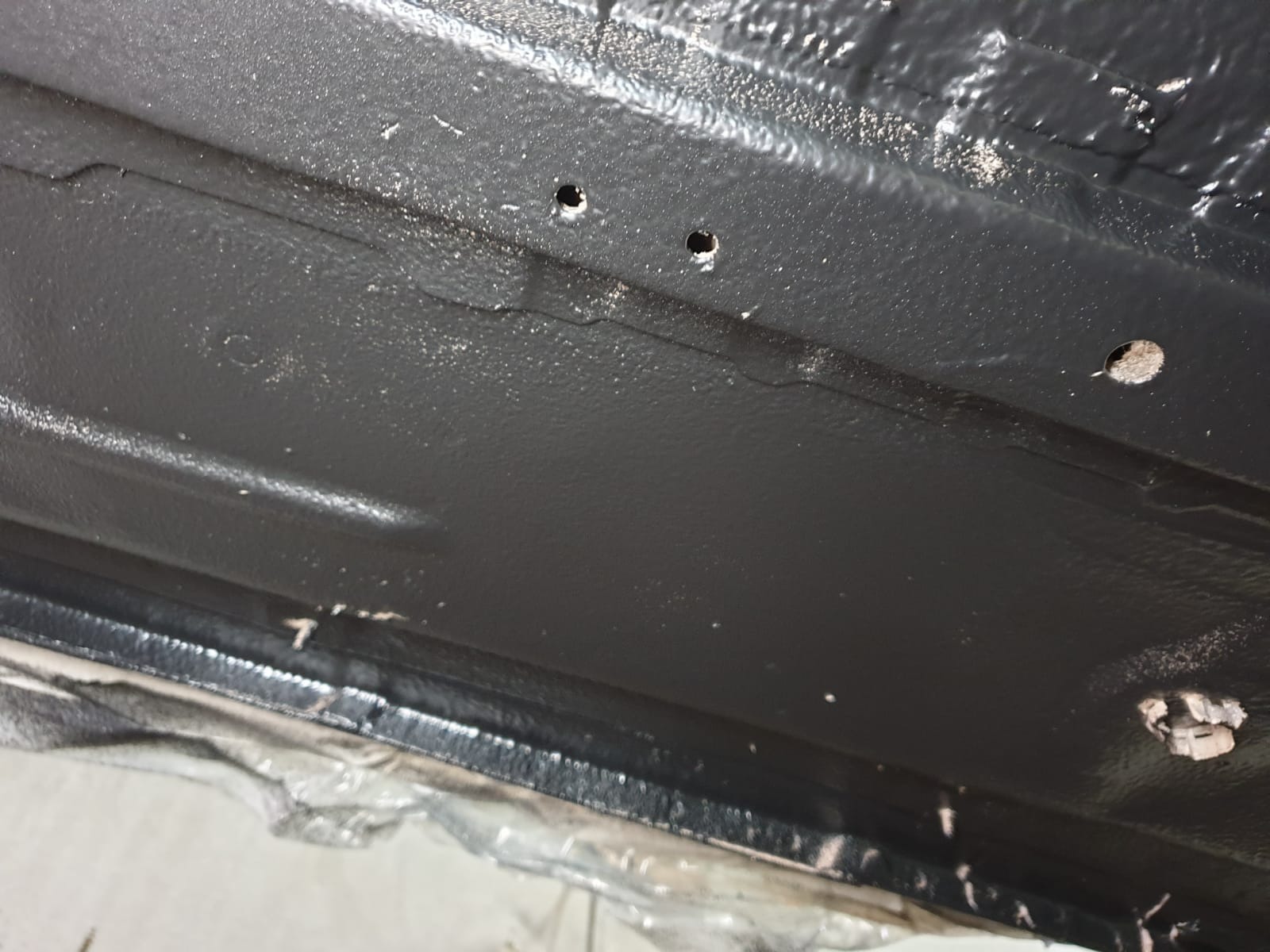 Wnętrze progu samochodu po zabezpieczeniu antykorozyjnym, widoczne otwory technologiczne i struktura nałożonej powłoki ochronnej.