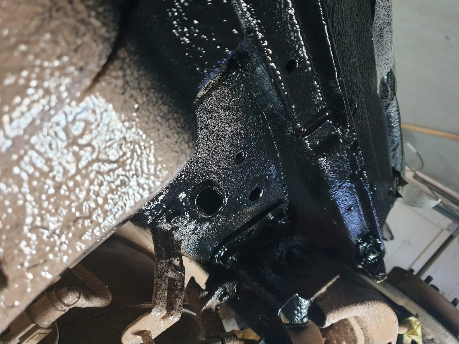 Spód samochodu po nałożeniu warstwy antykorozyjnej, widoczne elementy zawieszenia i metalowa konstrukcja pokryta czarną, błyszczącą powłoką. Fragmenty elementów nadal w kolorze rdzawym.