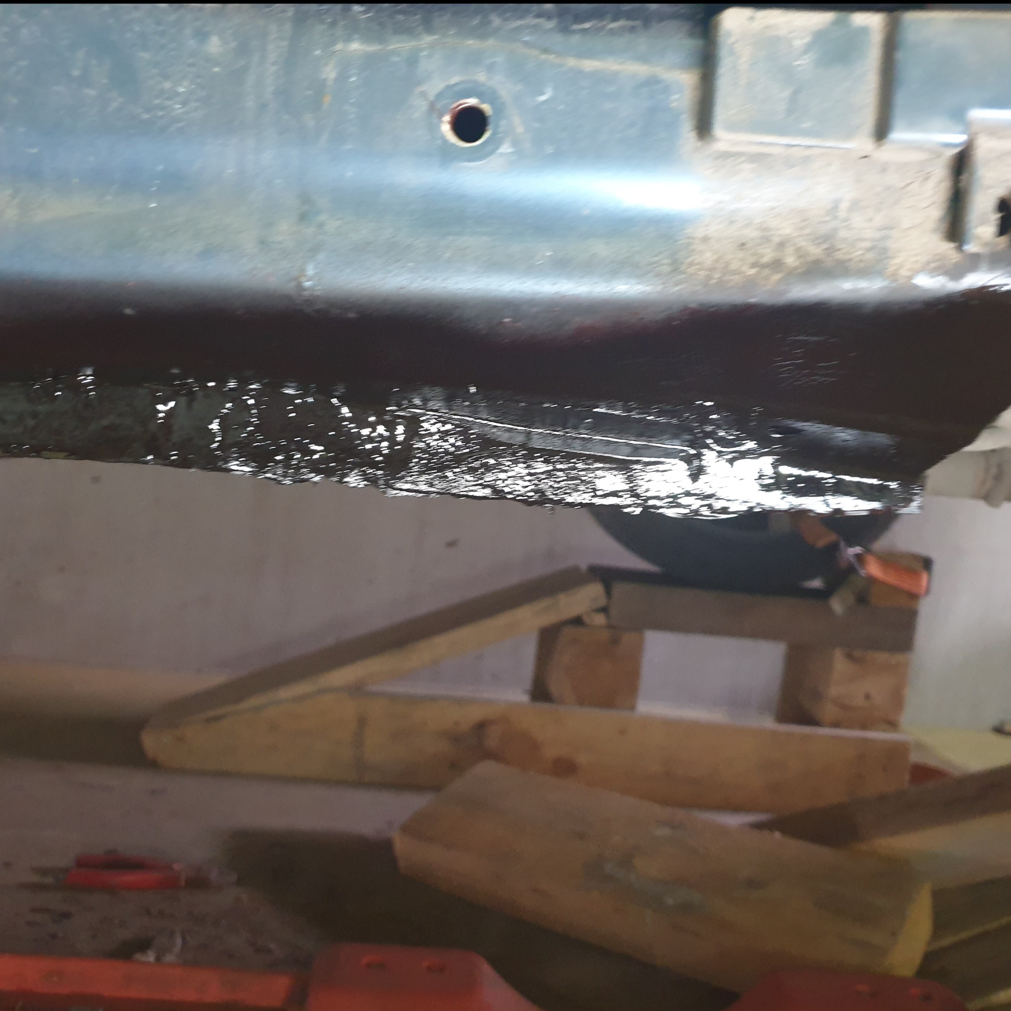 Spód samochodu zabezpieczony antykorozyjnie, widoczne drewniane podpory i elementy wyposażenia warsztatu.