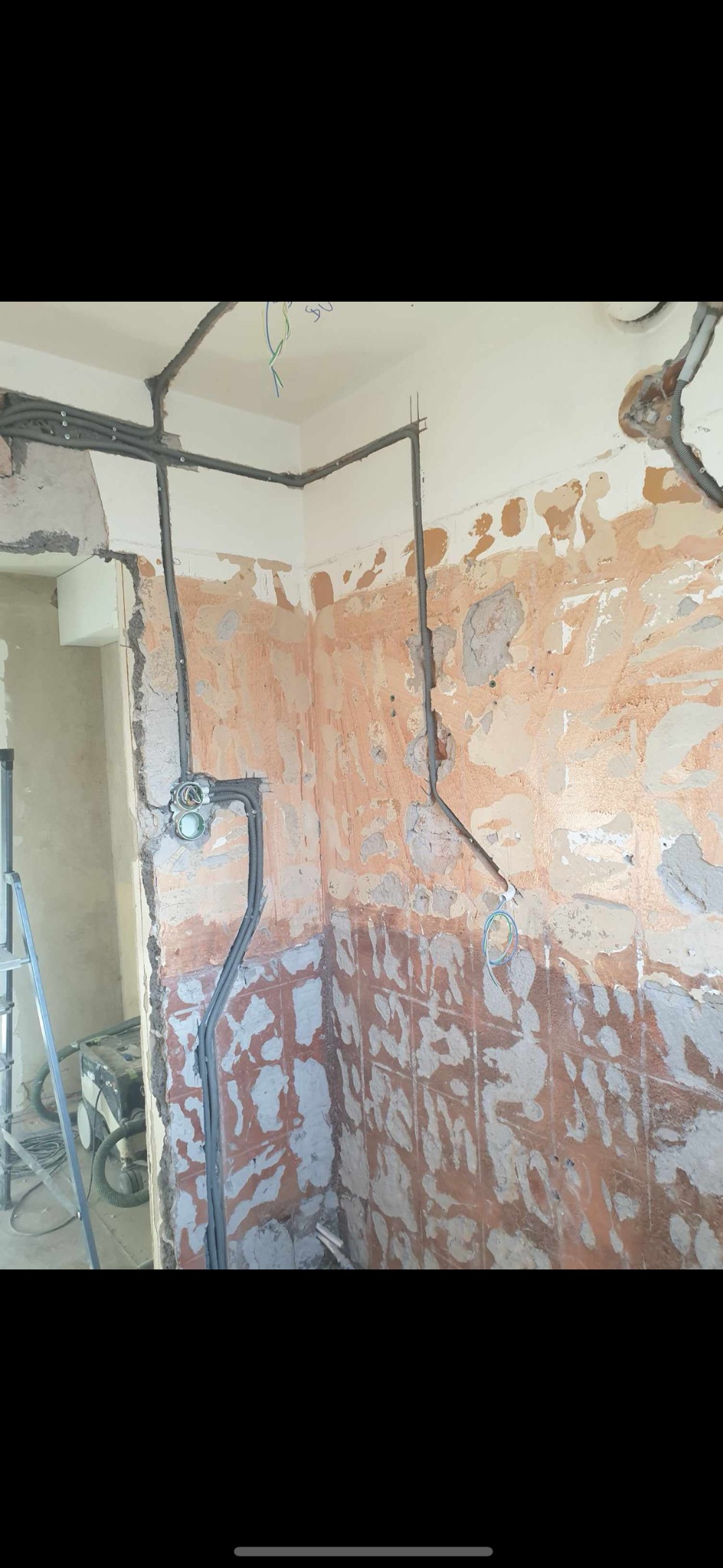 Szare rury w peszlu prowadzone po ścianach w trakcie remontu, widoczne puszki elektryczne i fragment drabiny.