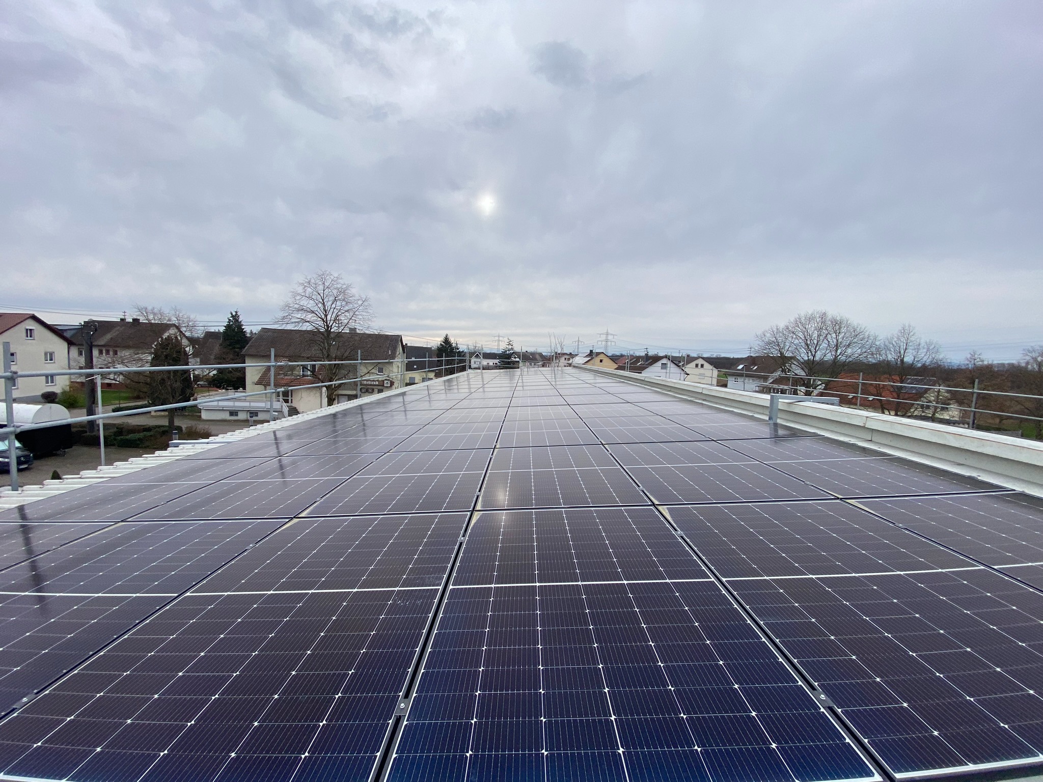 Instalacja fotowoltaiczna na płaskim dachu budynku mieszkalnego, widok z góry, pochmurne niebo.