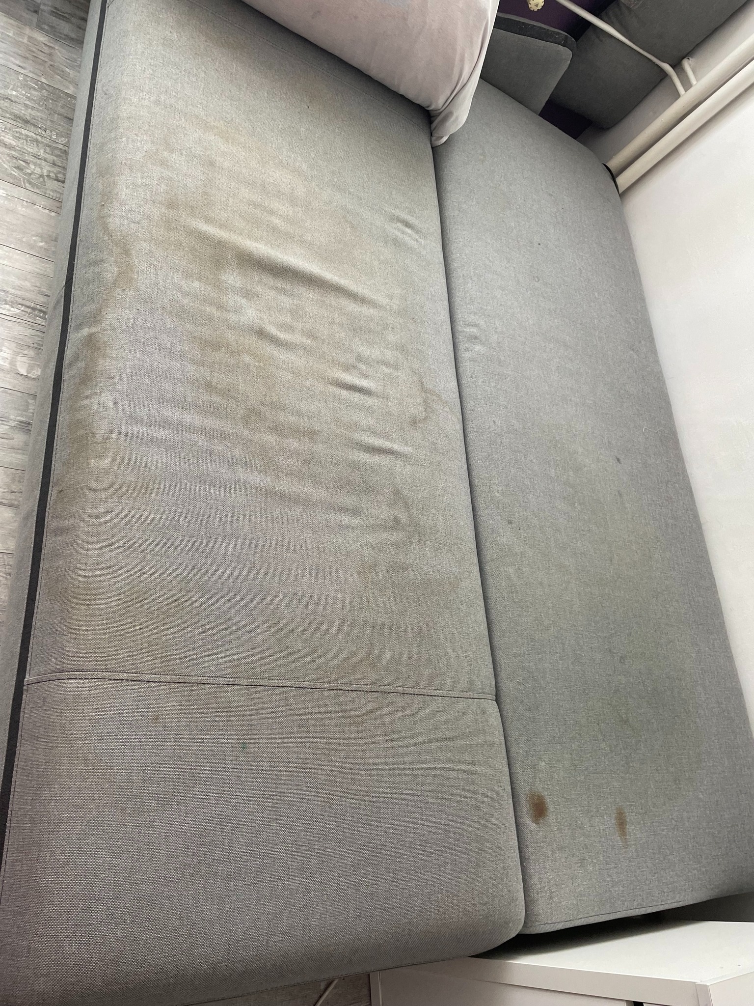 Szara kanapa z widocznymi plamami na tapicerce, widok z góry, przed czyszczeniem.