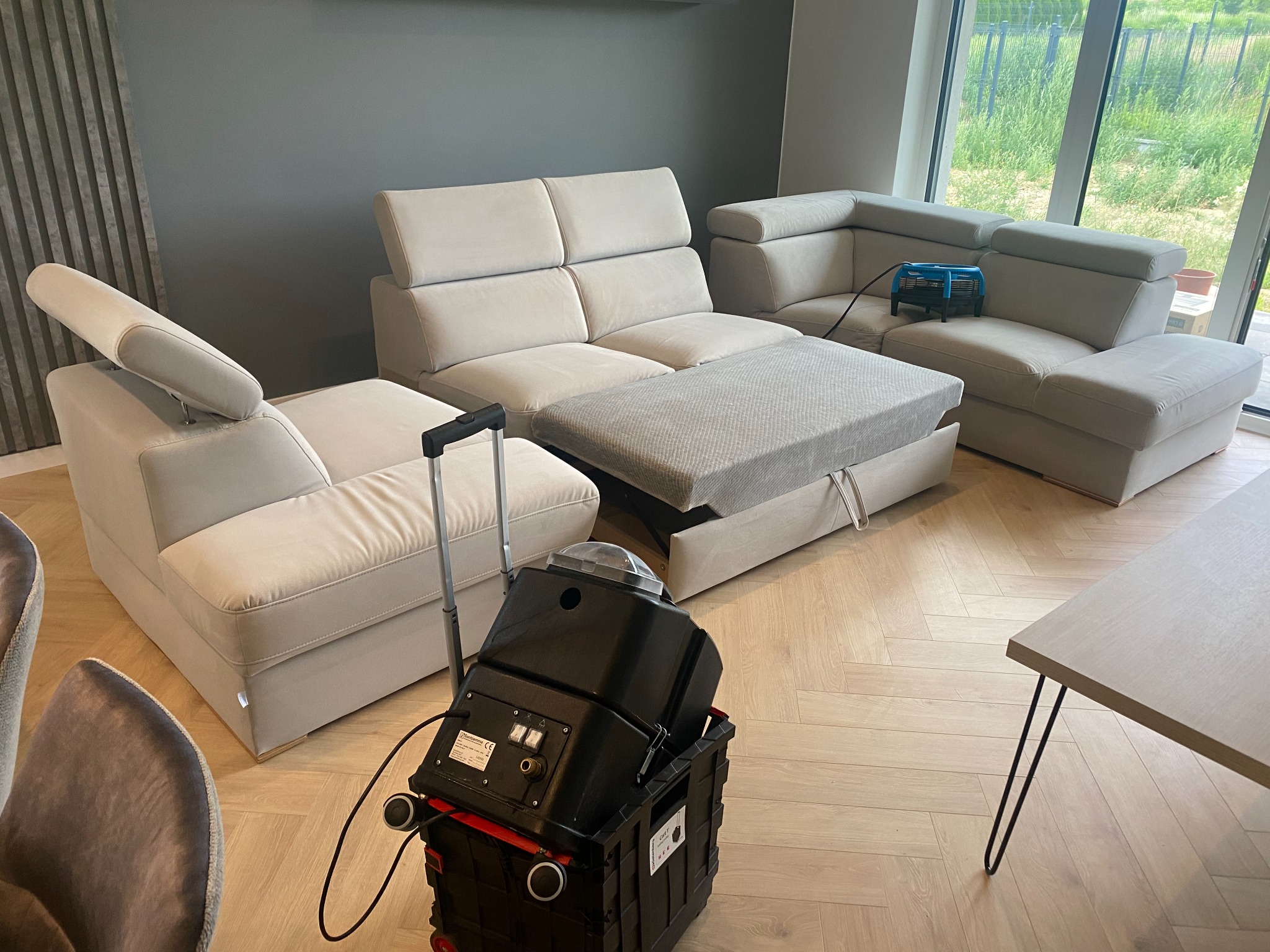 Jasna, modułowa kanapa z wysuwanym siedziskiem, suszarka i profesjonalny odkurzacz piorący na drewnianej podłodze w salonie podczas czyszczenia.