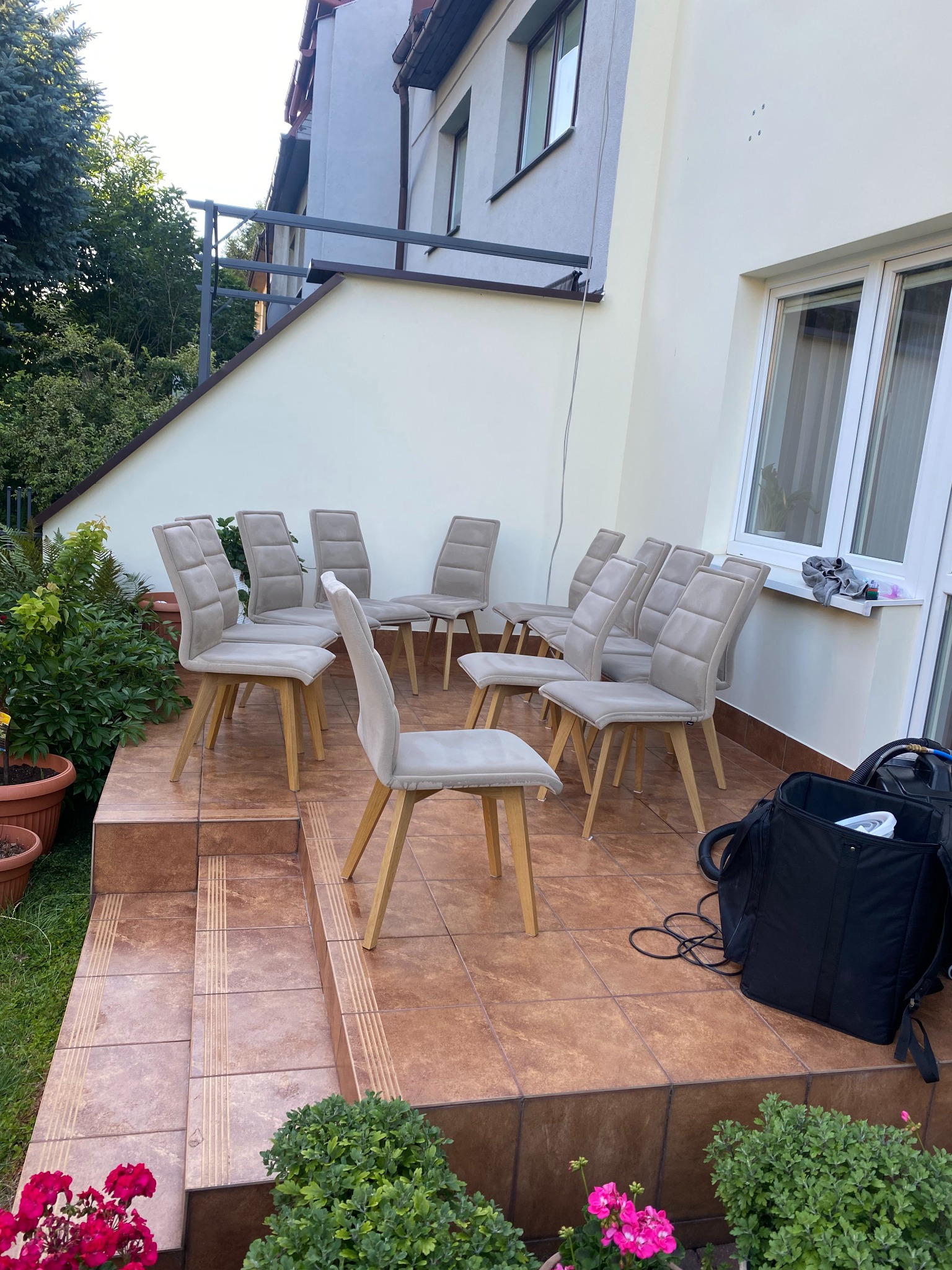 Ustawione na tarasie krzesła tapicerowane w odcieniach beżu, przygotowane do czyszczenia, obok widoczna torba z akcesoriami i wąż odkurzacza.