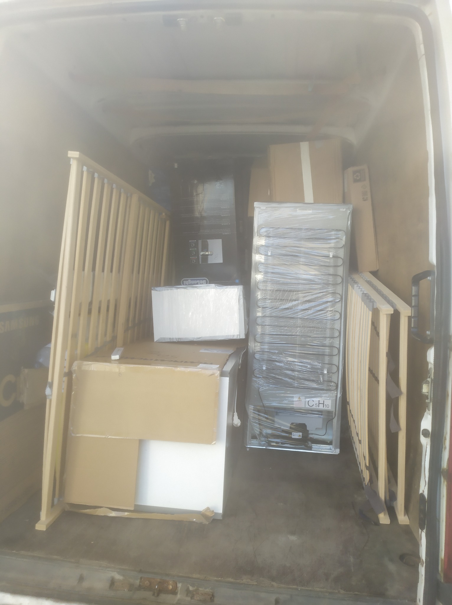 Wnętrze furgonetki załadowane kartonami, rozmontowanym łóżkiem dziecięcym i lodówką, przygotowane do transportu.