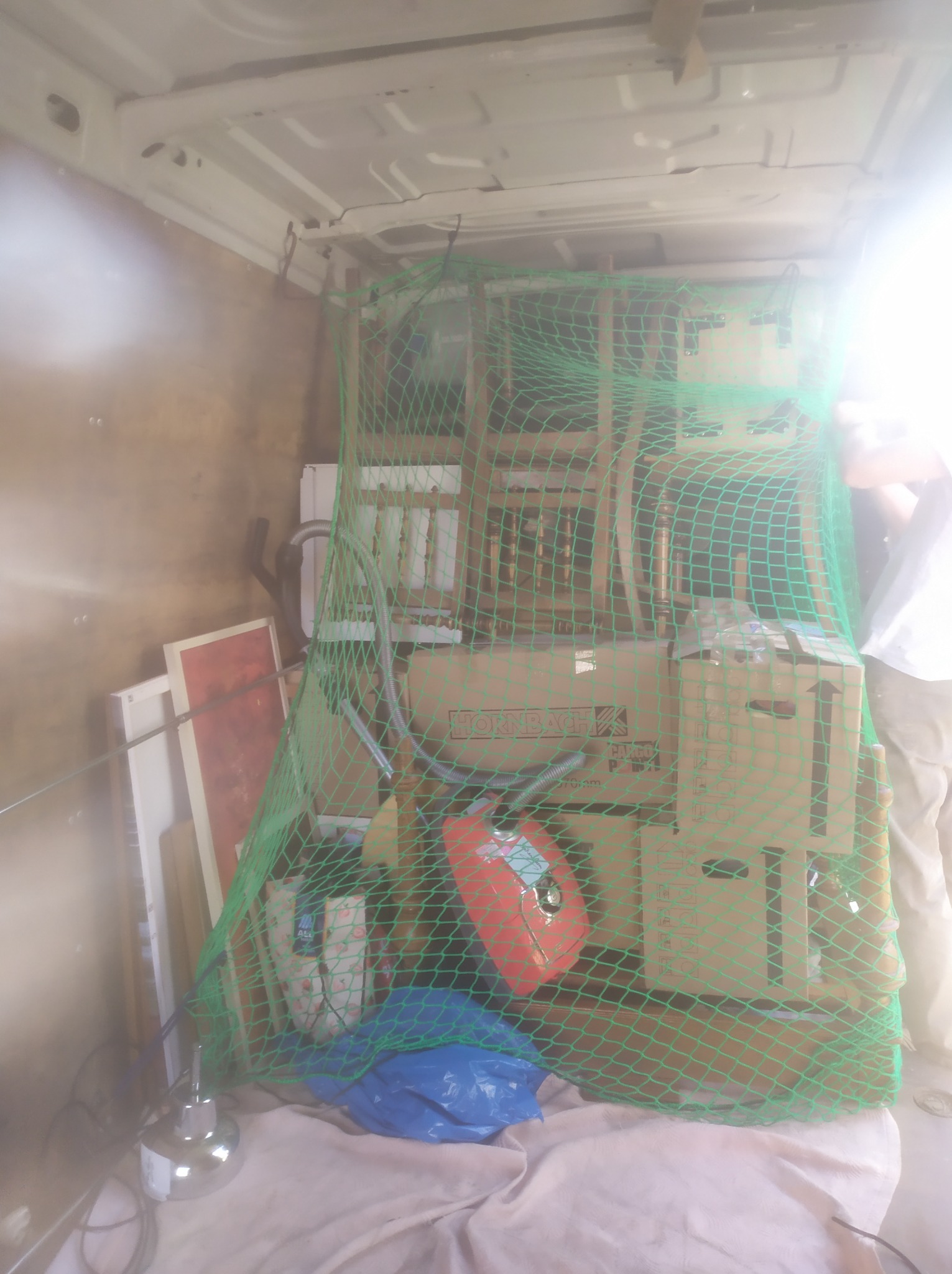 Wnętrze busa zabezpieczone zieloną siatką transportową, zawierające kartony, meble i inne przedmioty podczas przeprowadzki.