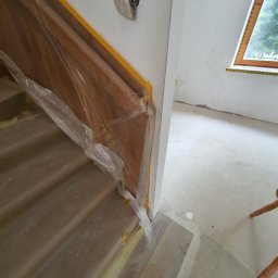 KARO-BUD Sławomir Kadleczek - Schody zabezpieczone folią i taśmą malarską podczas prac wykończeniowych, widoczne gniazdko elektryczne i okno w tle.