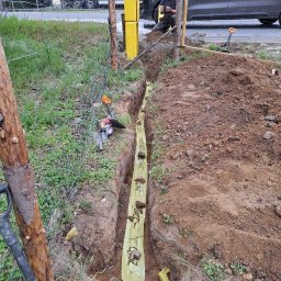 INSTALPRO Andrzej Kuczaj - Wykop pod rurę gazową zabezpieczony żółtą folią ochronną z napisem GAZ, widoczne narzędzia pracy, pracownik siedzący obok samochodu firmy zajmującej się instalacjami gazowymi.